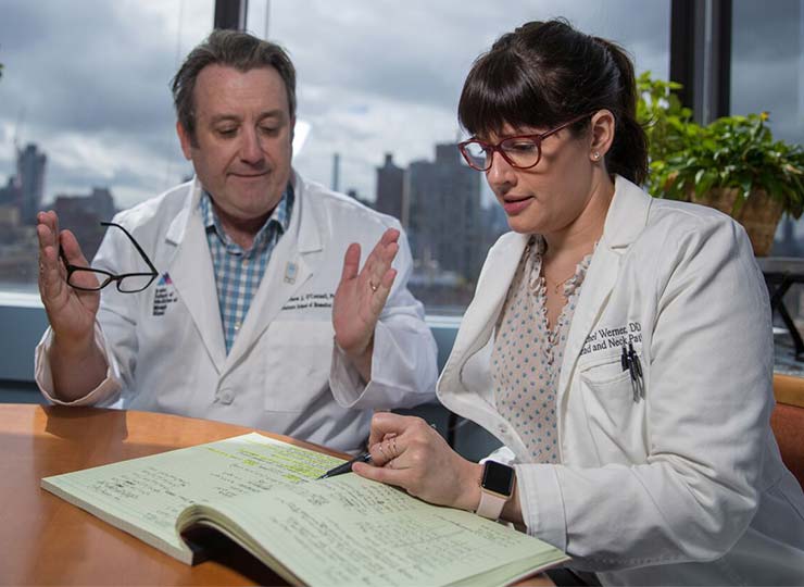 One doctor looking in book and another gesturing while speaking