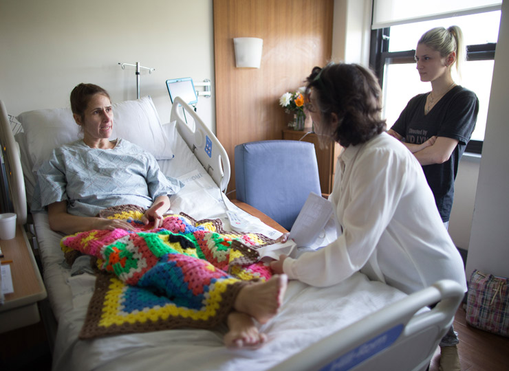 Two people visiting a patient in a hospital bed