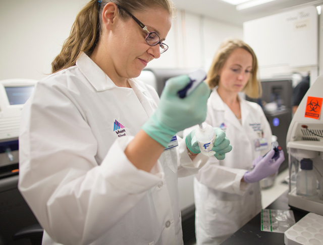 Two female researchers wearing white lab coats, working in lab